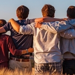 A group of four teenagers facing away from the camera in a rural field